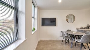 A modern dining area with a round table and chairs, a flat-screen TV mounted on the wall, and a window with blinds. - Host Stay 23 Waterside Place (Taunton)