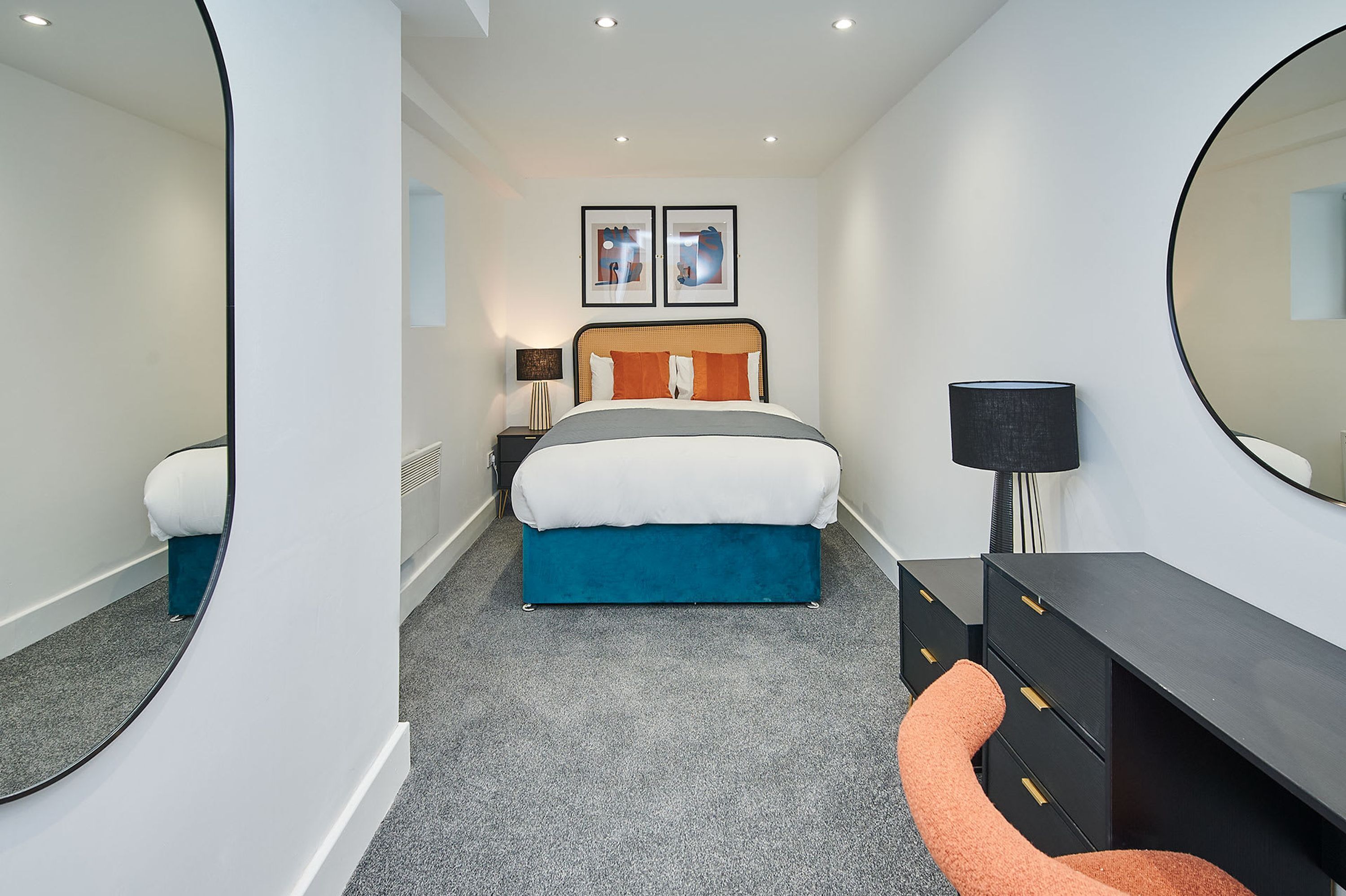 A bedroom with a bed, a dresser, a mirror, and two framed pictures on the wall.