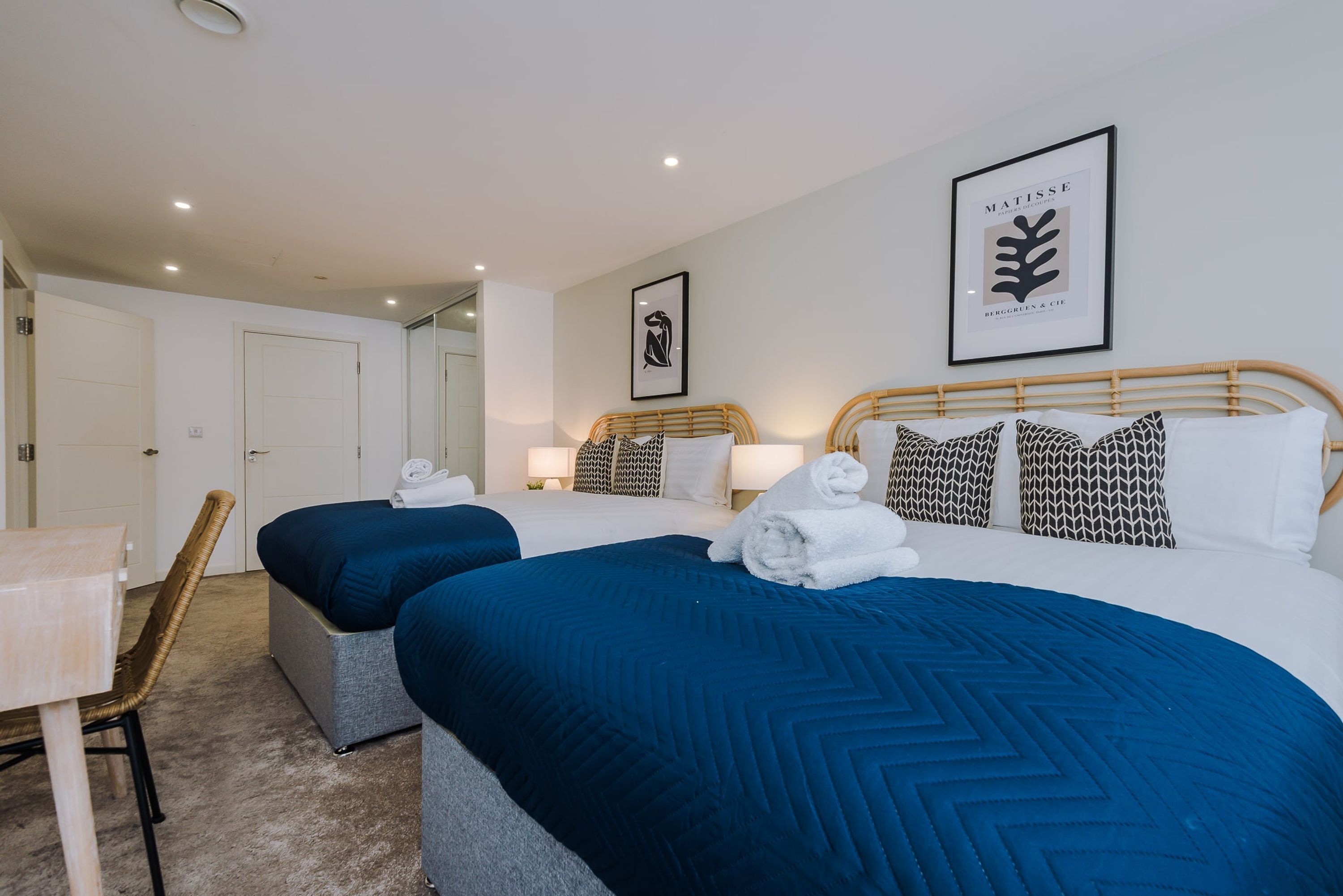 A hotel room with two single beds, a desk, and a chair.