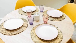 Una mesa de madera redonda con individuales tejidos, platos blancos y cristalería transparente.