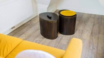 A room with a wooden floor, a white radiator, and two dark cylindrical objects with yellow tops.