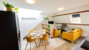 Un salón moderno con comedor, sofás amarillos, una estantería de madera y un cuadro mural con vistas a la ciudad.
