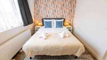 Un lit bien fait, avec une couette blanche et deux oreillers, un tapis à motifs et un mur orné d’un motif géométrique.