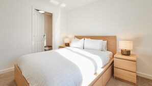 A neatly made bed with white linens, two bedside tables with lamps, and a wooden headboard. - Host Stay Aronora Guest House (Blaydon on Tyne)