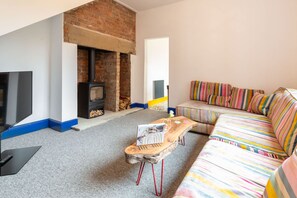 A cozy living room with a brick fireplace, a flat-screen TV, a striped sofa, and a wooden coffee table. - Host Stay Temple Gardens (Lincoln)