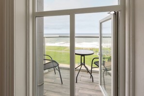 Een glazen deur die leidt naar een balkon met uitzicht op de oceaan en een kleine ronde tafel met twee stoelen.