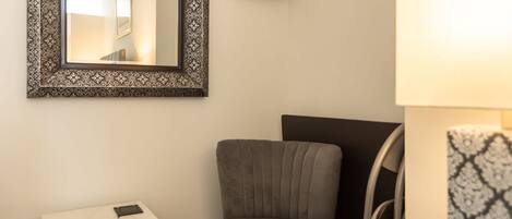 A room with a grey upholstered chair, a small white table with a marble top, and a patterned side table.