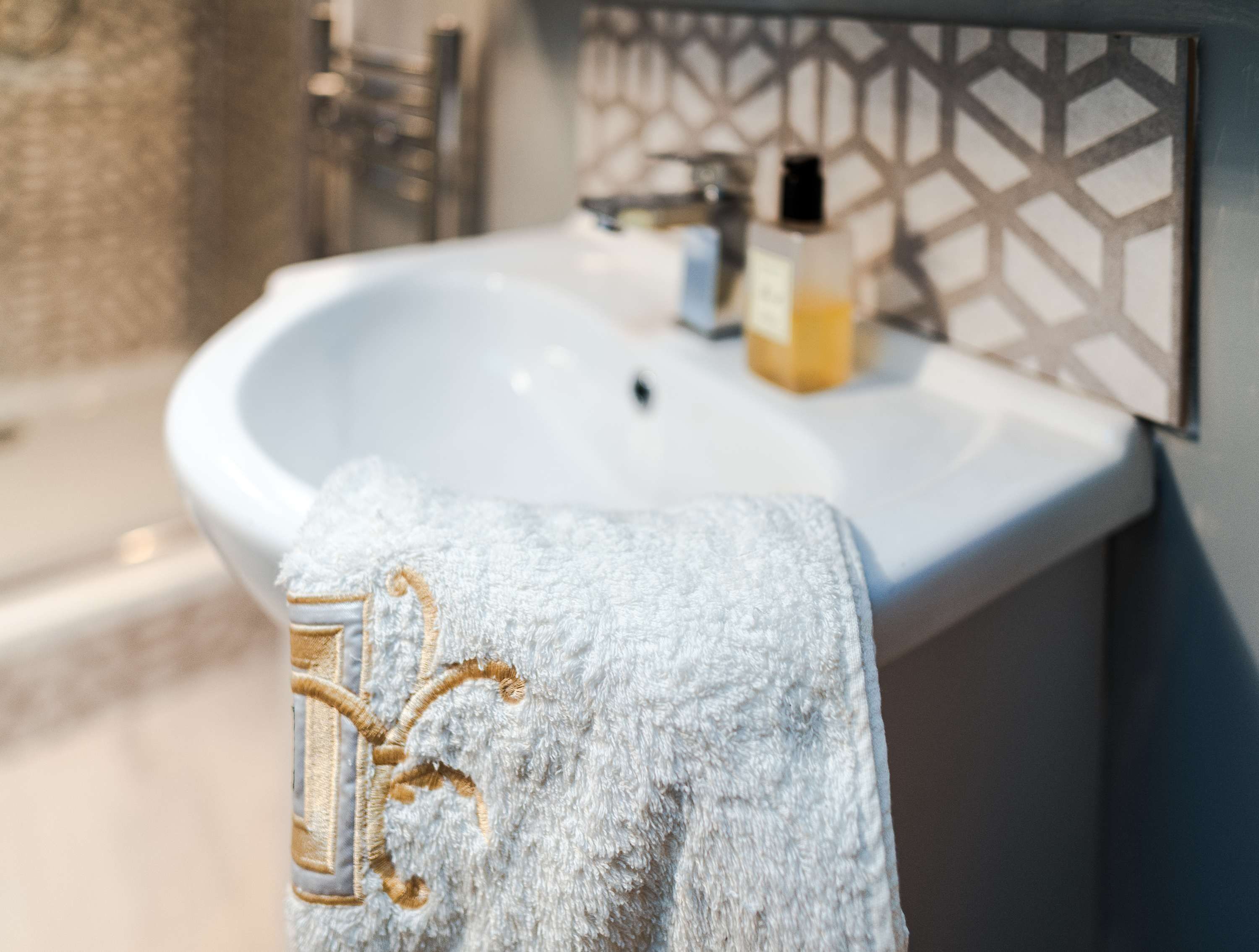 A bathroom with a white sink, a towel with a gold embroidered design, and a geometric patterned wall.