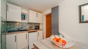 A compact kitchen with white cabinets, a microwave, and a sink. There's a wooden door and a white basket with apples on the counter. - Host Stay Pied-a-terre at Manor View (Bury)