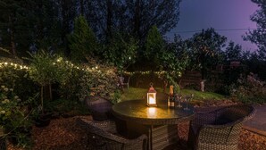 An outdoor dining area with wicker chairs and a round table, surrounded by foliage and string lights. - Host Stay Pied-a-terre at Manor View (Bury)