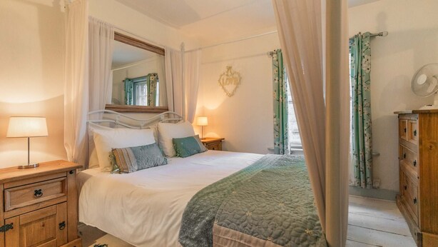 A bedroom with a bed, bedside tables, a mirror, a dresser, and a chandelier. - Host Stay Fishermans Cottage (Cromer)