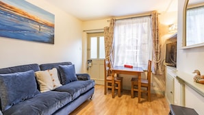 A living room with a blue sofa, a wooden dining table, and a painting on the wall. - Host Stay Fishermans Cottage (Cromer)