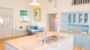 A modern kitchen with a central island, white cabinetry, and pendant lighting. - Host Stay Boathouse Barn (Norwich)
