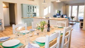 A dining area with a wooden table set for four, white chairs, and a light blue cabinet in the background. - Host Stay Boathouse Barn (Norwich)