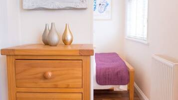 A bedroom with a wooden dresser, a bed with a purple blanket, and a framed picture on the wall.