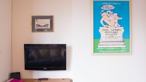 Ett rum med en tv som är monterad på väggen, ett skrivbord i trä med en rosa pärm och en inramad tavla ovanför skrivbordet.