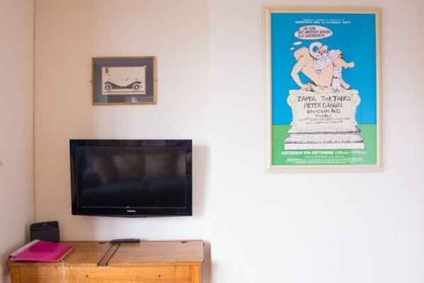 A room with a television mounted on the wall, a wooden desk with a pink folder, and a framed picture above the desk. - Host Stay Apartment 3 York Terrace (Norwich)