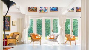 A bright room with white walls, large windows, wicker chairs, and a floor lamp. - Host Stay Hen Barn (Norwich)