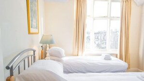 Habitación de hotel con dos camas, una ventana con cortinas, una lámpara y un cuadro en la pared.