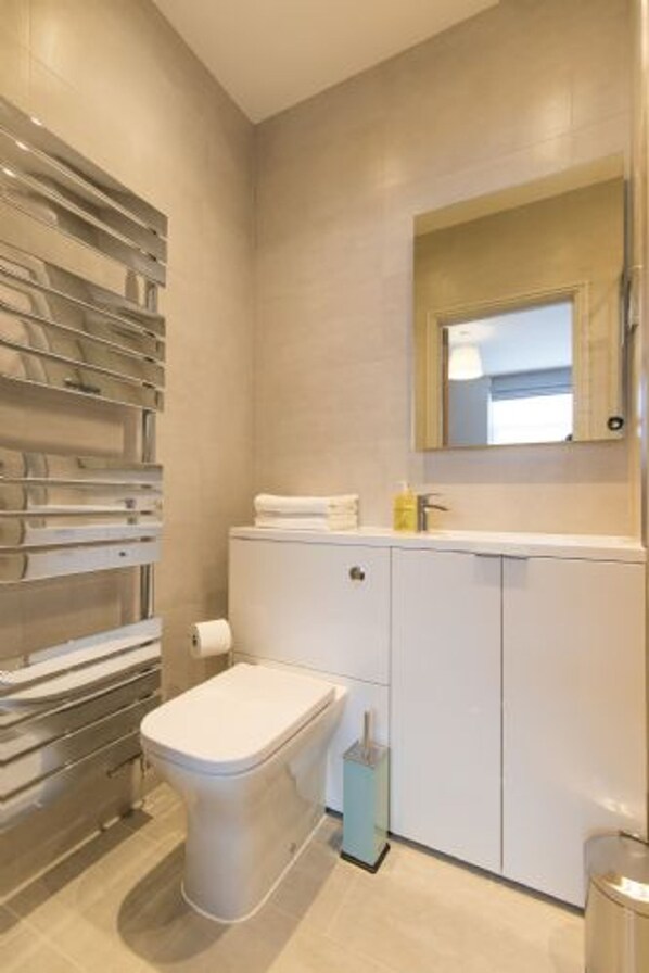 A modern bathroom with a toilet, a sink with a mirror, and a towel rack. - Host Stay The Old Antique Shop (Holt)