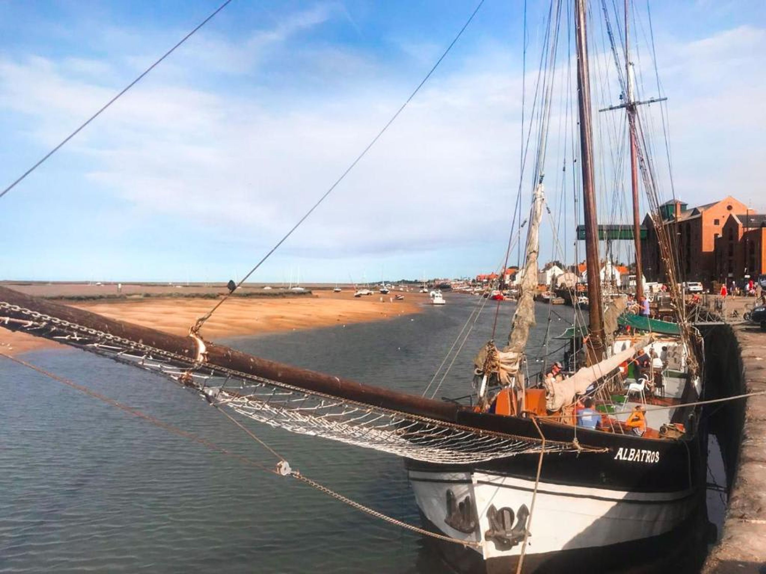 En båd ved navn 'ALBATROS' ligger ved kaj i en havn med en sandstrand og bygninger i baggrunden.