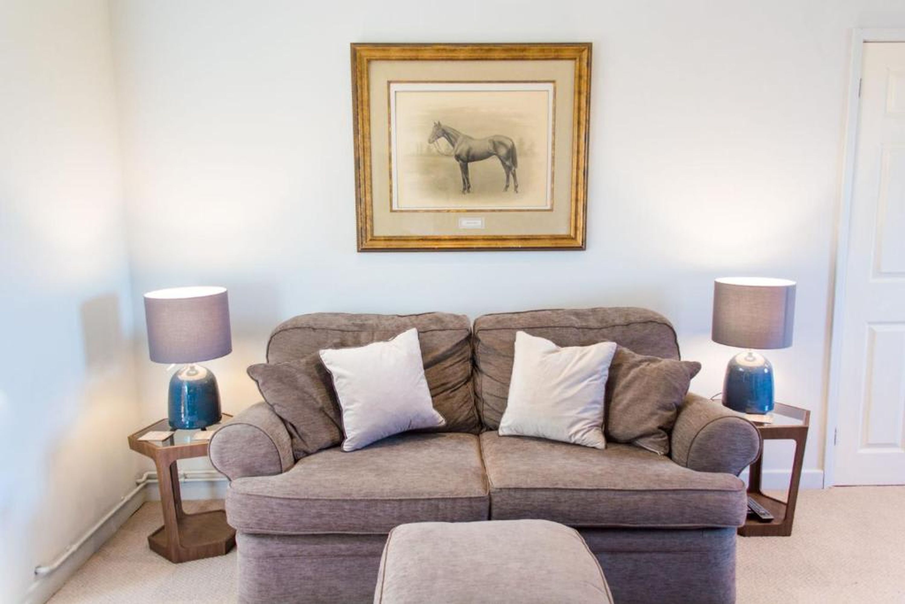 Un salón moderno con un sofá gris, dos mesitas de noche con lámparas y un cuadro enmarcado de un caballo en la pared.