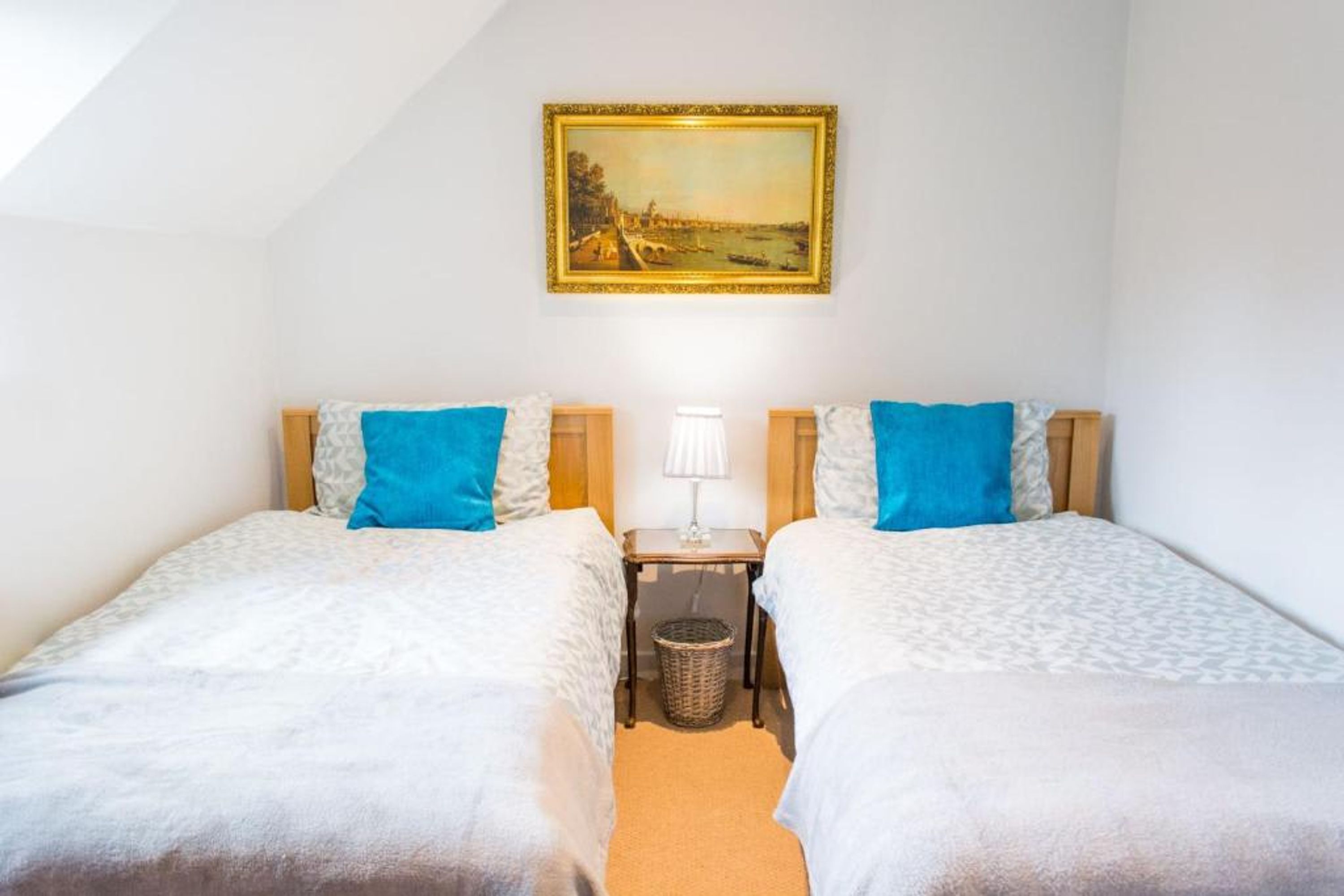 Une chambre double avec deux lits, une table de chevet, une lampe, un tableau et une petite corbeille à déchets.
