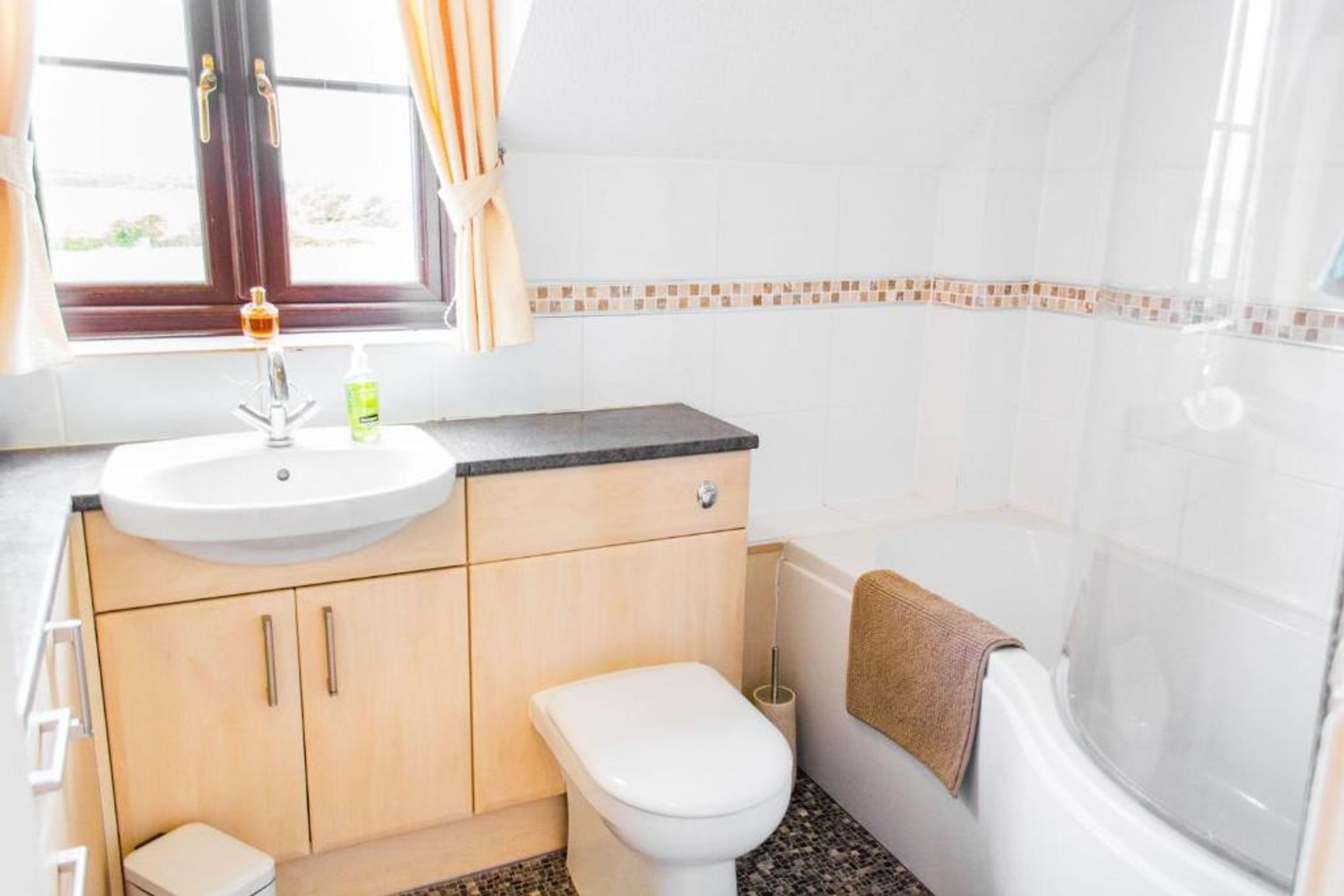 Une salle de bain avec un lavabo blanc, des meubles en bois, des toilettes et une baignoire.