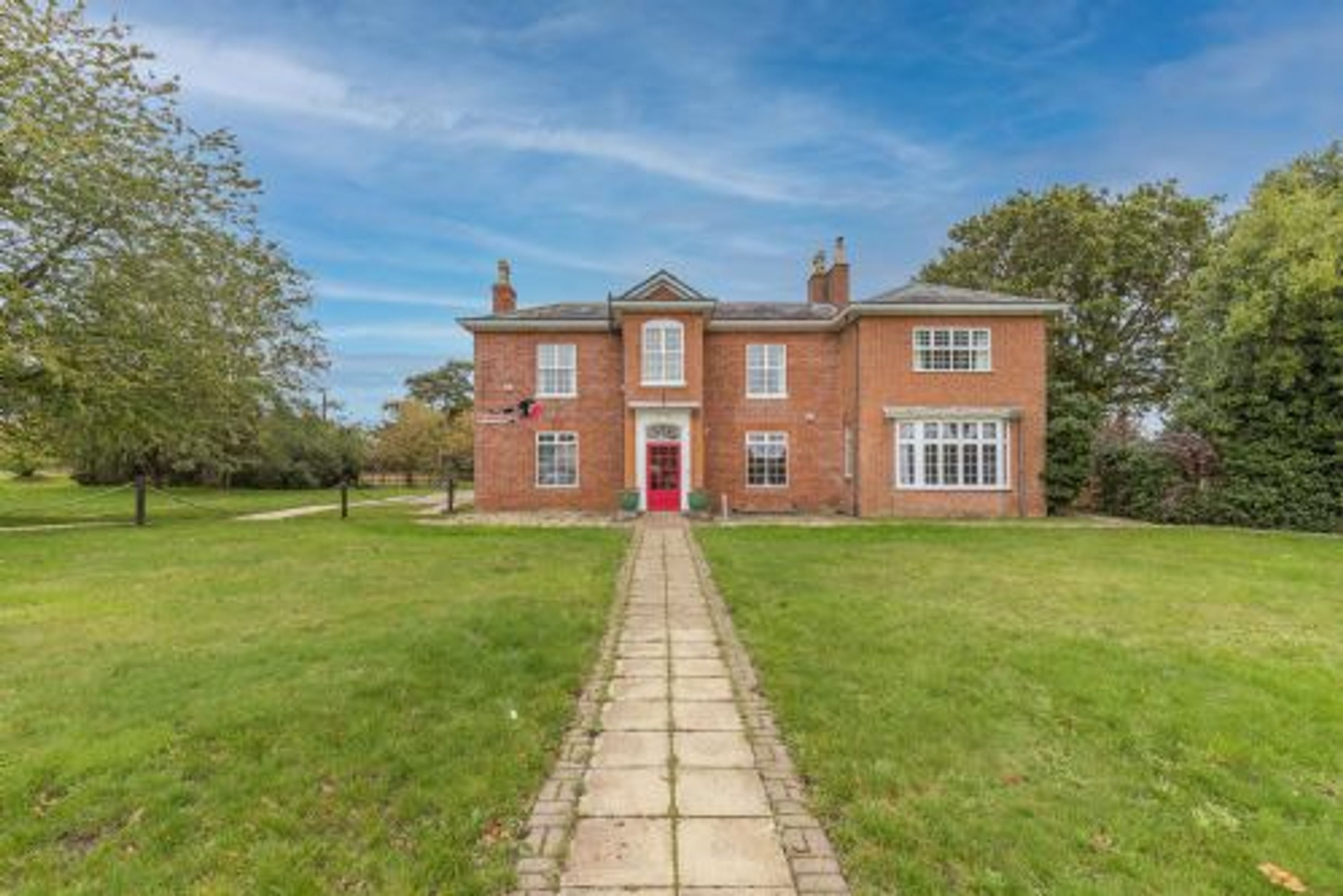 A brick house with a central red door, a paved pathway leading to it, and a well-maintained lawn.