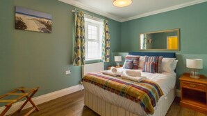 Une chambre à coucher avec un lit, une fenêtre avec des rideaux, un tableau au mur et une table de chevet avec une lampe.