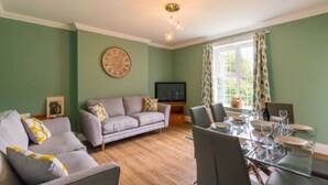 Un salon comprenant un canapé, des fauteuils, une table à manger dressée pour quatre personnes et un téléviseur.