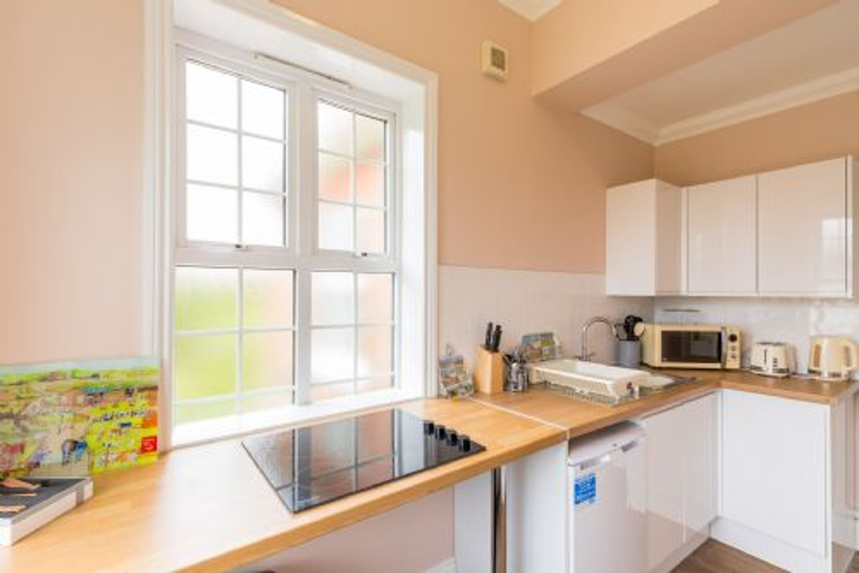 A modern kitchen with white cabinets, a microwave, a toaster, and a window with a view of greenery.