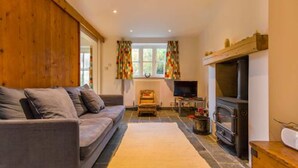 A cozy living room with a sofa, a television, a fireplace, and a window with curtains.