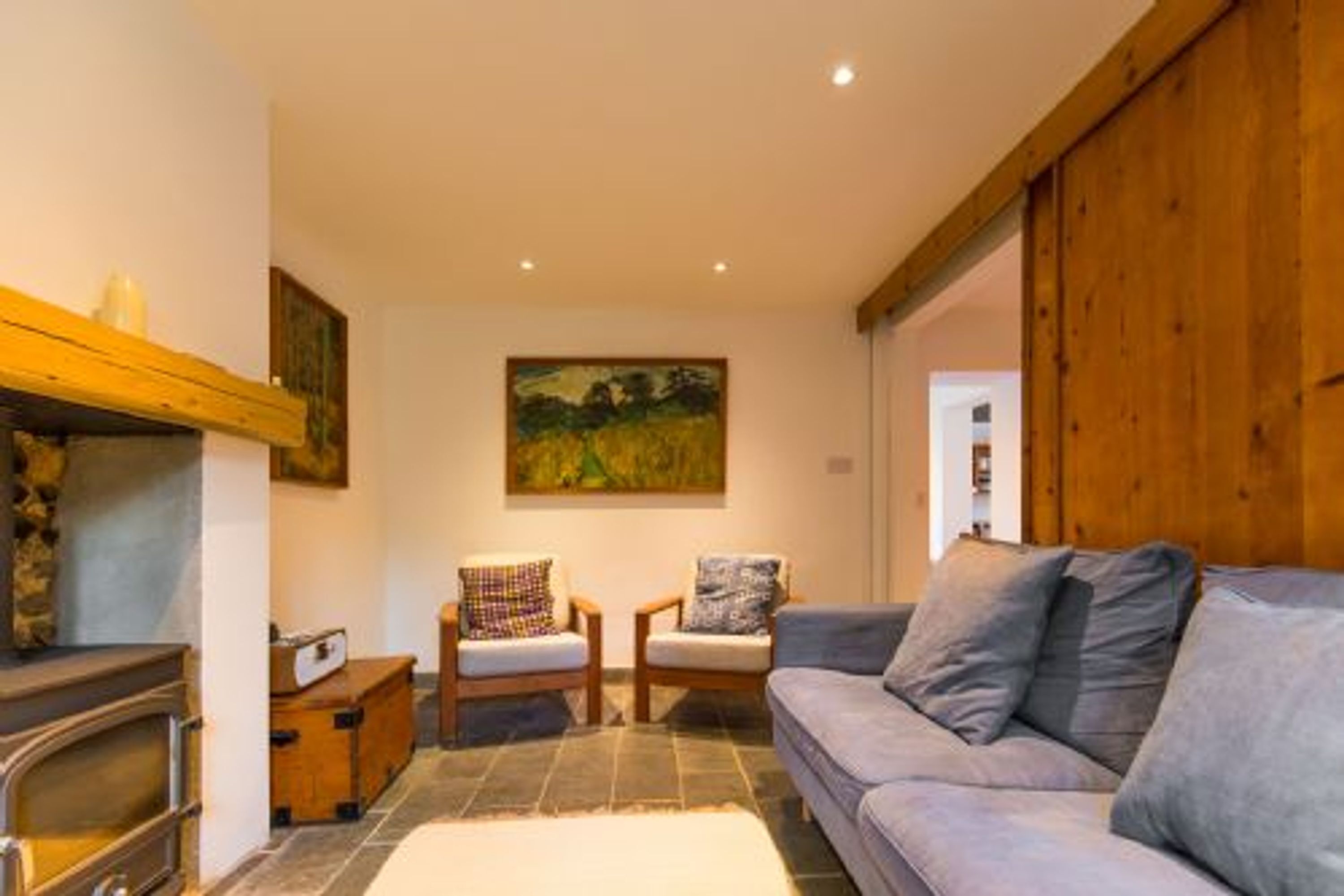Uma sala de estar aconchegante com lareira, um sofá, duas poltronas e um quadro na parede.