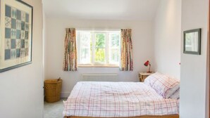 A bedroom with a bed, a window with curtains, a radiator, and a framed picture on the wall.