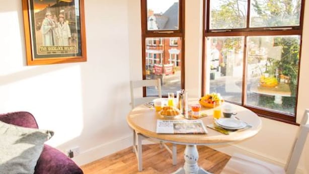 A dining area with a table set for breakfast, a poster on the wall, and a view of the street outside.