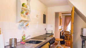 La cuisine est dotée d’un plan de travail noir, d’un évier en acier inoxydable et d’un égouttoir à vaisselle. On y trouve également une table et des chaises en bois dans l’espace repas attenant.