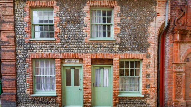 Un bâtiment à la façade en pierre et aux portes vertes, portant l’inscription « FISHERMANS COTTAGE ».