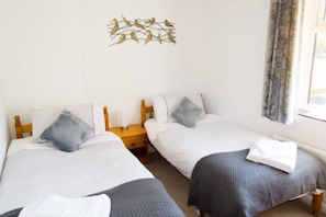 A hotel room with two single beds, a wooden headboard, a nightstand, and a decorative wall piece. - Host Stay Quayside Cottage (Norwich)
