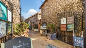 A narrow alleyway with stone buildings, a sign for 'Tess Ainy Gallery', and a chalkboard advertising afternoon teas and breakfast.