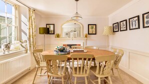 A dining room with a round table, six chairs, a chandelier, a fireplace, and framed artwork on the wall.