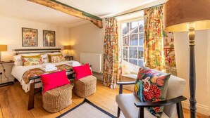 A cozy bedroom with a bed, two side tables, a chair, and a window with curtains.