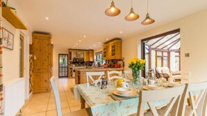 A spacious kitchen with wooden cabinets, a dining table set for four, and pendant lighting. - Host Stay Four Seasons (Norwich)