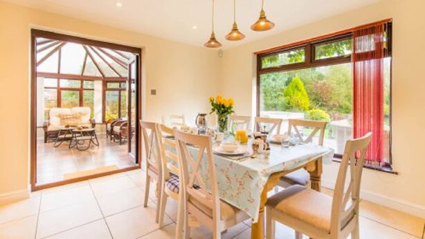 A dining area with a table set for four, a sofa in the background, and a view of greenery outside. - Host Stay Four Seasons (Norwich)