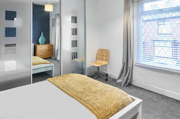 A modern bedroom with a bed, a wooden dresser, a chair, and a window with blinds. - Host Stay Thurstane Street (Bolton)