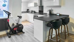 A modern kitchen with white cabinets, a central island, and a Reebok exercise bike. - Host Stay Thurstane Street (Bolton)