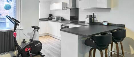 A modern kitchen with white cabinets, a central island, and a Reebok exercise bike.