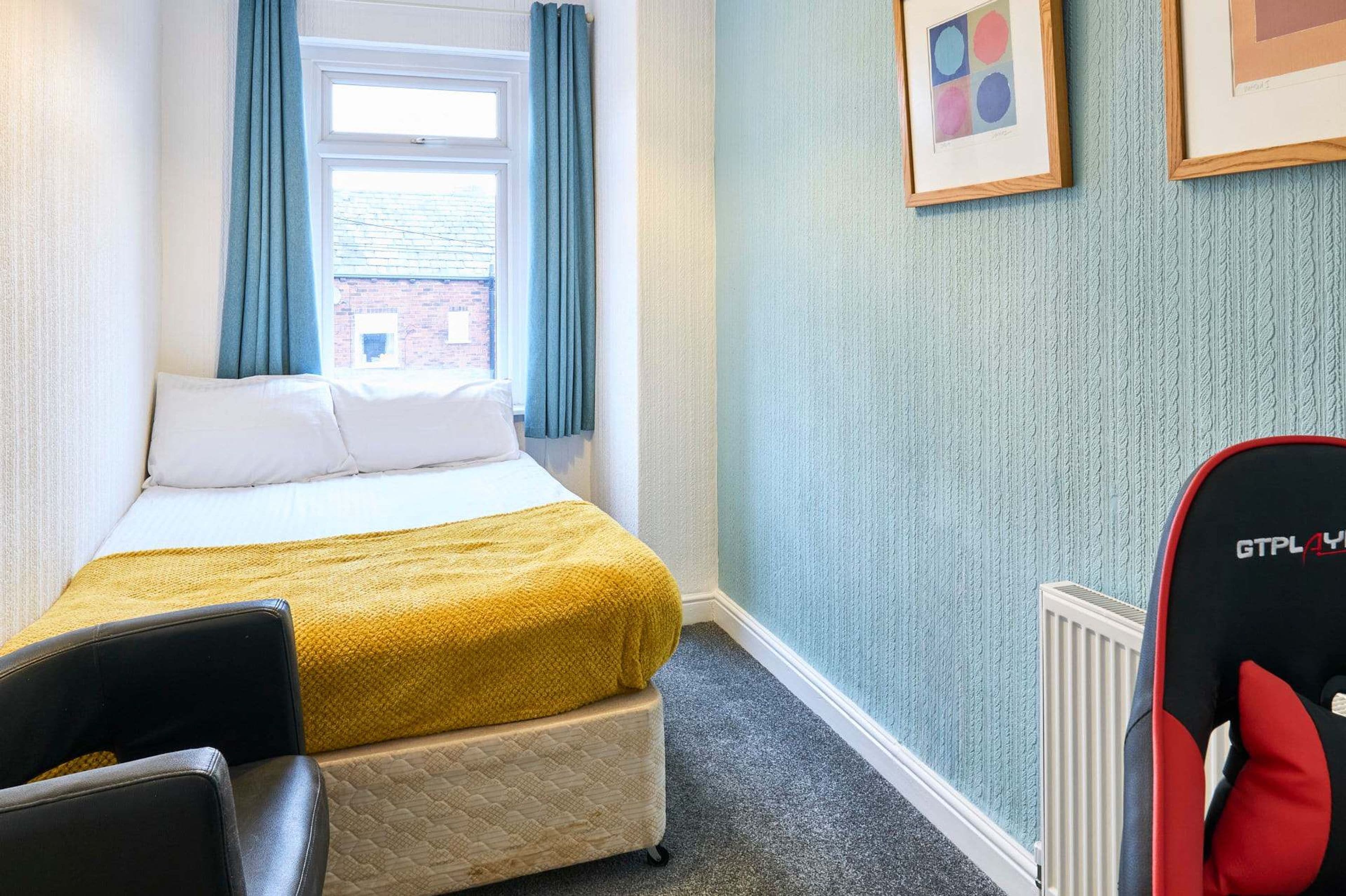 A hotel room with a bed, a chair, a radiator, and a window with curtains.
