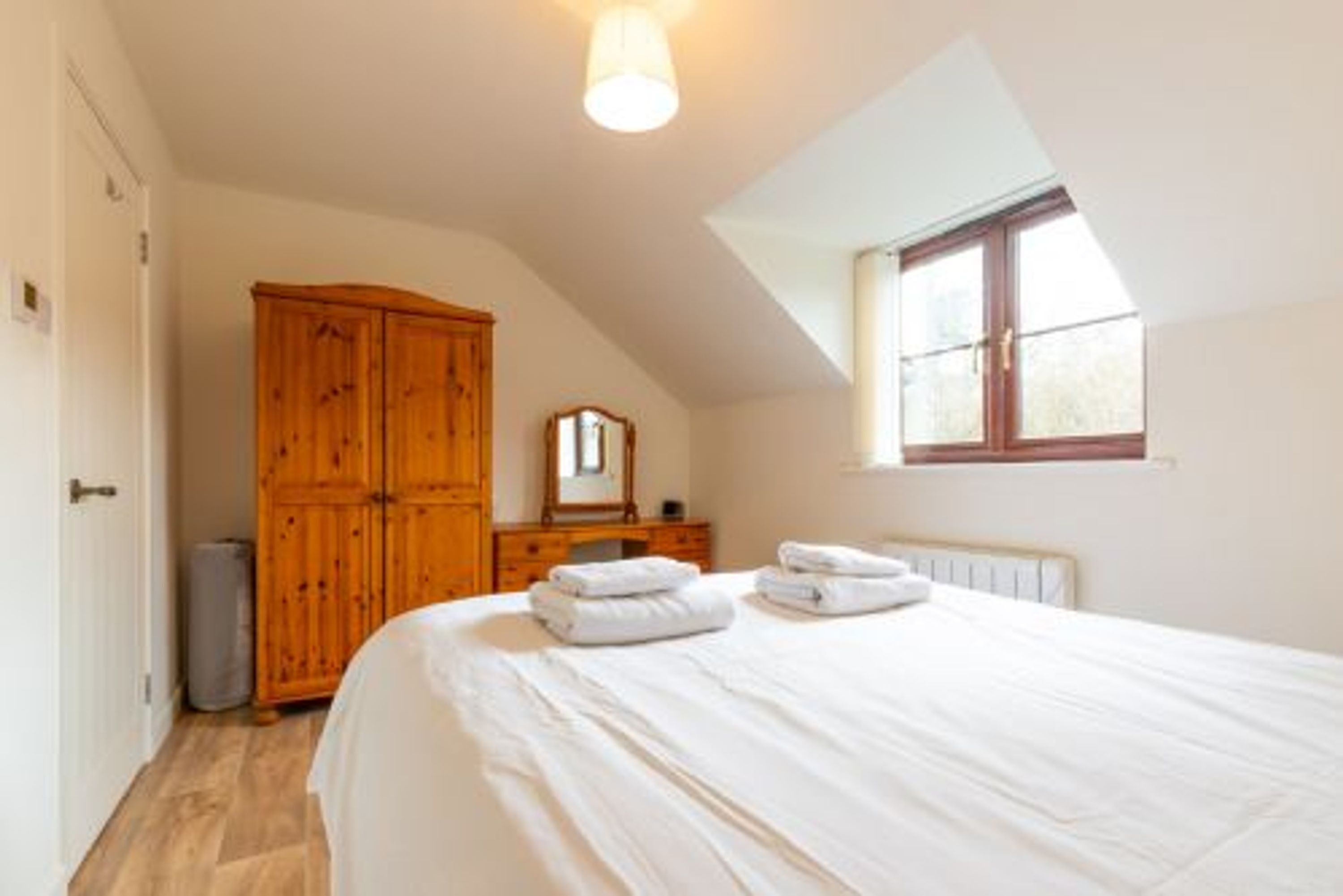 A bedroom with a large bed, a wooden wardrobe, a radiator, and a window with curtains.