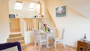 Una habitación acogedora con un sofá morado, una mesa de comedor blanca con sillas y una escalera que sube a un nivel superior.